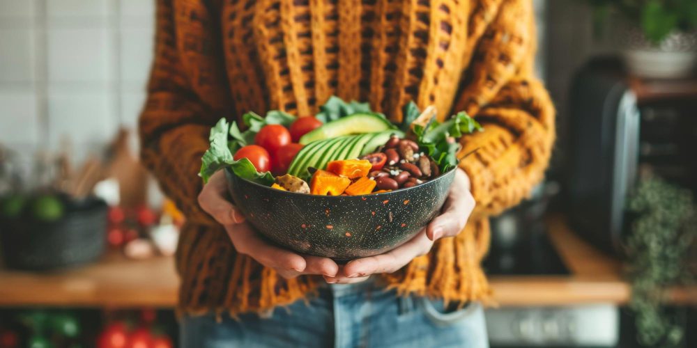 Persona sosteniendo un plato con alimentos saludables como verduras, legumbres y aguacate representando hábitos saludables
