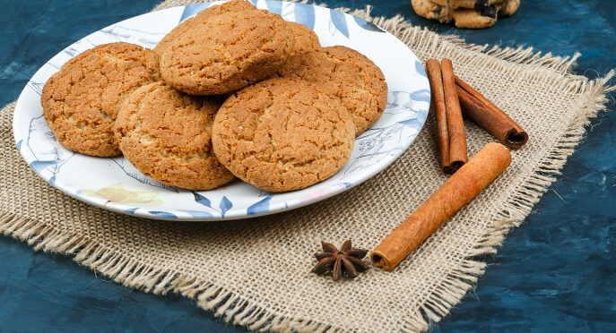 Galletas fitness de avena sin azúcar servidas en un plato sobre una superficie rústica, acompañadas de canela, ideales como snack saludable.