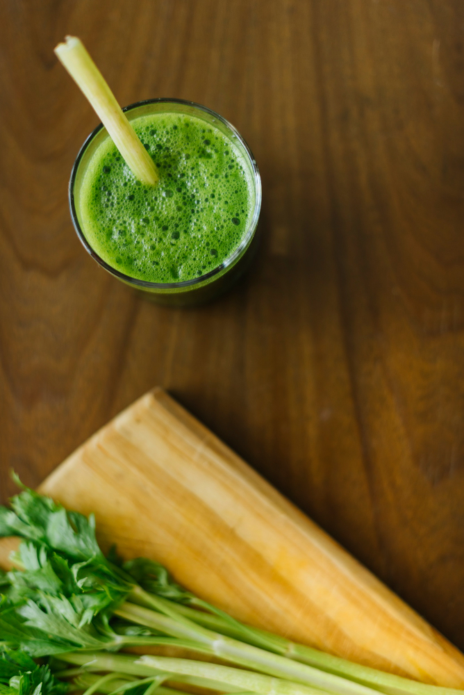 Vaso de zumo verde digestivo con apio, hinojo y jengibre sobre mesa de madera