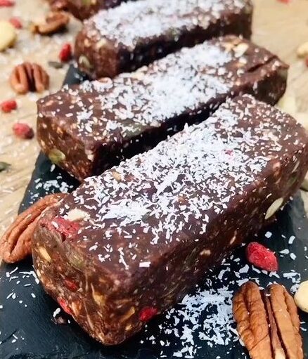 Barritas energeticas caseras hechas con ingredientes naturales, sin azúcar añadido, decoradas con coco rallado y frutos secos, presentadas sobre una tabla de cocina.