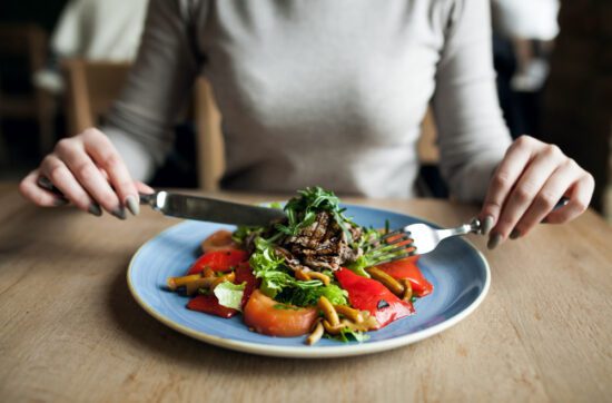 Mujer comiendo ensalada saludable, ejemplo de exceso de alimentos crudos que puede provocar hinchazón y gases