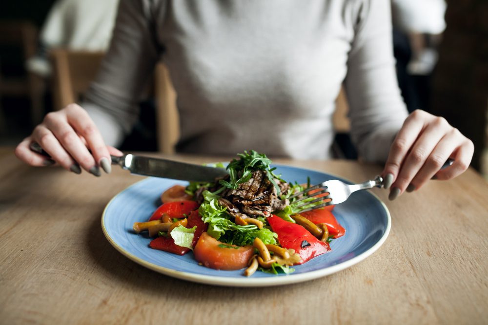 Mujer comiendo ensalada saludable, ejemplo de exceso de alimentos crudos que puede provocar hinchazón y gases