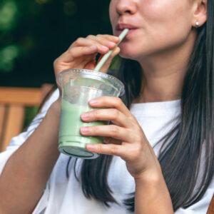 Mujer bebiendo zumo verde natural de vegetales con pajilla al aire libre