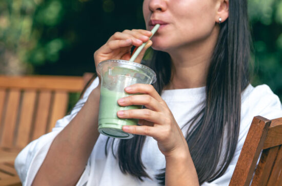 Mujer bebiendo zumo verde natural de vegetales con pajilla al aire libre
