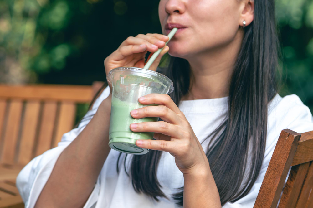 Mujer bebiendo zumo verde natural de vegetales con pajilla al aire libre