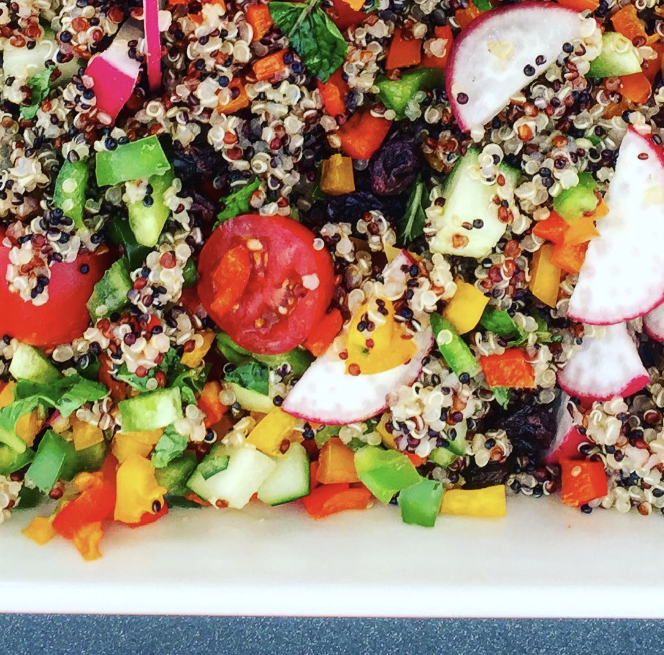 Ensalada de quinoa tricolor con pimientos, pepino, rábano, tomate cherry, uvas pasas y hierbas frescas, aliñada con vinagreta de limón y aceite de oliva.