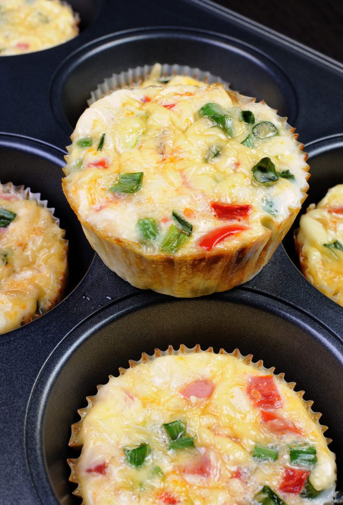Muffins salados de verduras y huevo recién horneados con pimiento rojo, cebolla y albahaca en bandeja de horno