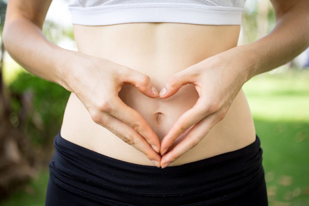 Mujer formando un corazón con las manos sobre el abdomen, representando la salud intestinal y los beneficios de la fibra en el sistema digestivo.