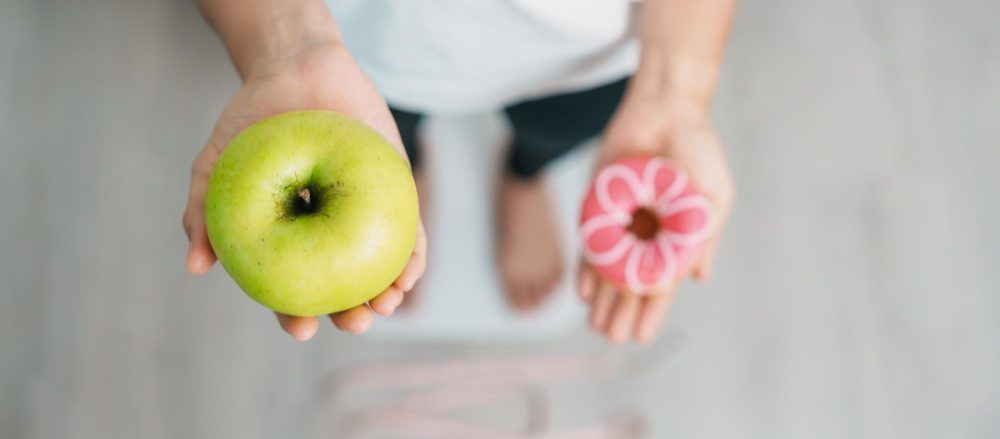 Mujer comparando una manzana saludable y un donut como elección para mejorar la fertilidad natural