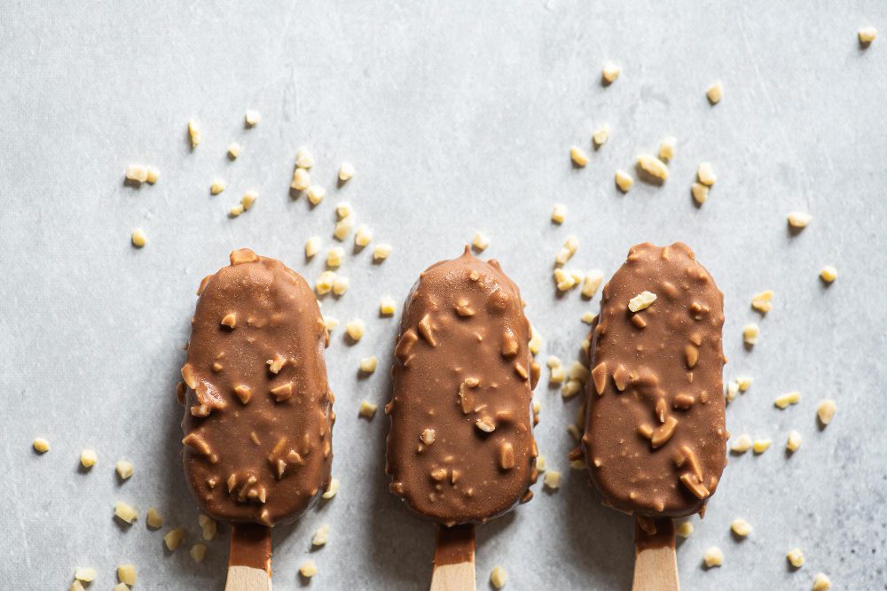 Helado proteico casero cubierto con chocolate y almendras sobre fondo gris